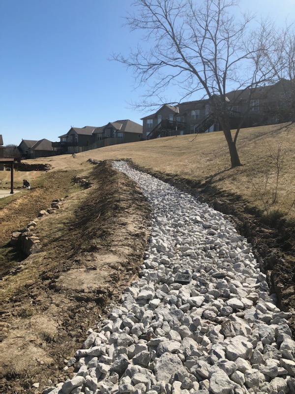 Wide view of finished drainage channel running down hillside — Lee's Summit, MO