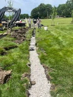 JLB installs French drain — excavator digs trench, gravel laid for drainage in Van Meter, IA