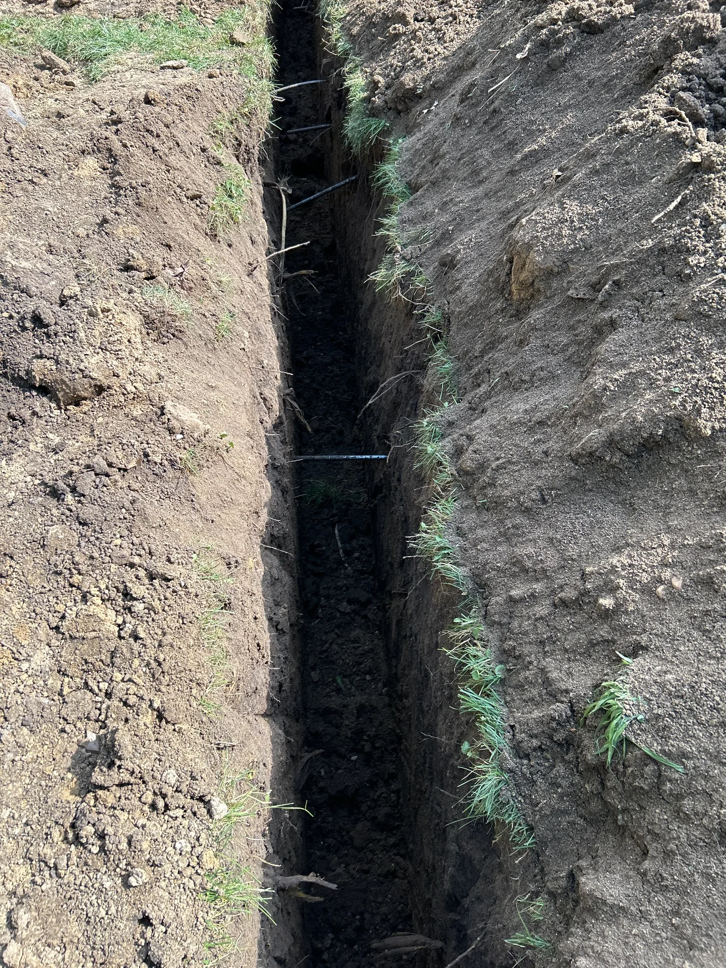 Exterior trench exposing bowing wall at full footer depth — wall anchor installation, Manson