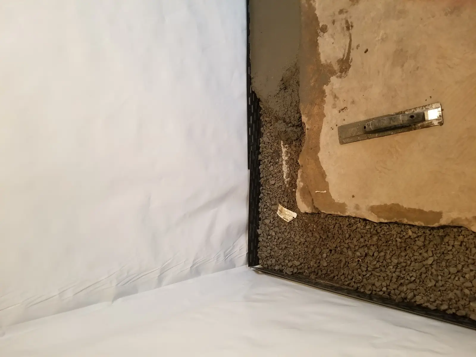 Drain gravel at the base of a basement wall beside a white liner